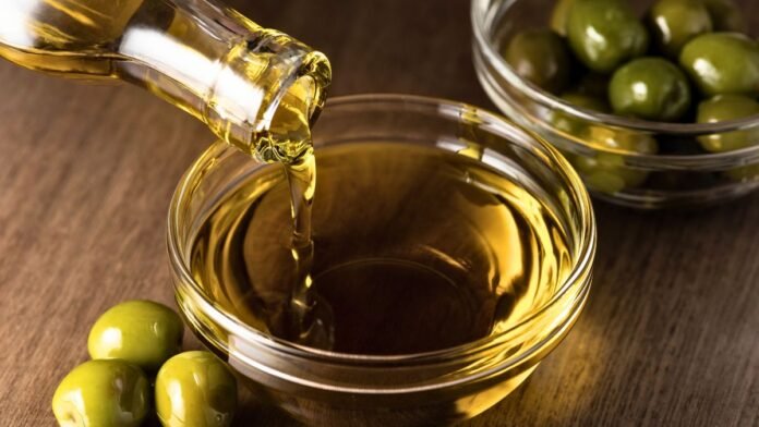 Aceite de oliva vertiéndose en un cuenco junto a aceitunas verdes